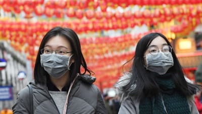 Två kvinnor går på en gata i London dekorerad med kinesiska dekorationer. Båda bär munskydd.