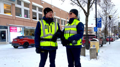 En man och en kvinna i reflexvästar står på en trottoar.