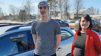 En tonåring och kvinna intill en bil. 