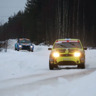 Kaksi ralliautoa ajaa talvisella tiellä peräkkäin.