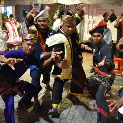 En grupp festklädda malaysiska män tittar mot kameran och intar olika kampställningar.