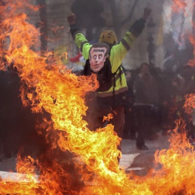 En demonstrant med en Macron-mask bland brinnande barrikader på Champs-Élysées. 