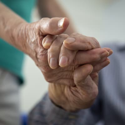 Två äldre som håller varandra i hand. Händerna visas i närbild.