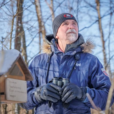 Fågelskådaren Juhani Hannila står med en kikare vid ett vintermatningsställe för fåglar.