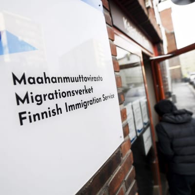 Seinällä on kyltti, jossa lukee "Maahanmuuttovirasto". Taustalla ihminen menee sisään ovesta.
