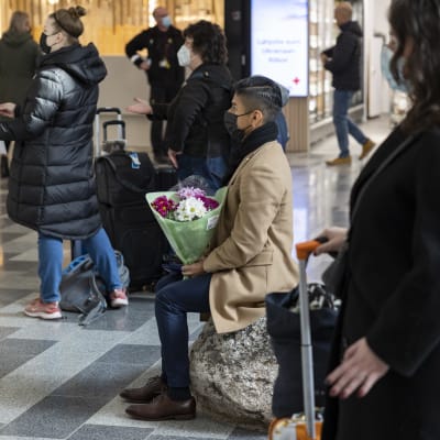 Henkilö odottaa saapuvaa kumppaniaan kukkakimppu kädessä Helsingin lentokentällä.