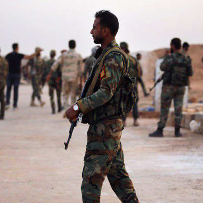 En syrisk soldat spankulerar beväpnad, utan huvudbonad.