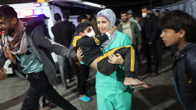 Nainen kantaa loukkaantunutta lasta kiiruhtavassa väkijoukossa. 