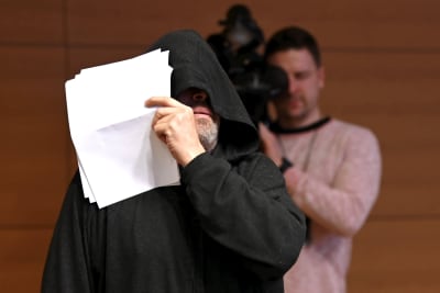 Mika Moring gömmer sitt ansikte med en huva och en pappersbunt på sin rättegång 23.12.2022.