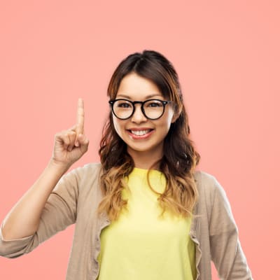 En ung kvinna med glasögon håller upp sitt ena pekfinger. 