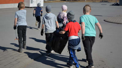Sex barn springer på en parkering med sopsäckar och griptänger.