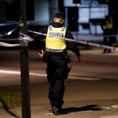 En svensk polis har ryggen mot kameran och står inför ett avstängt område i Göteborg efter en dödsskjutning i juli 2021.