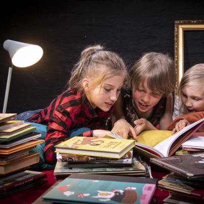 Tre barn läser böcker tillsammans.