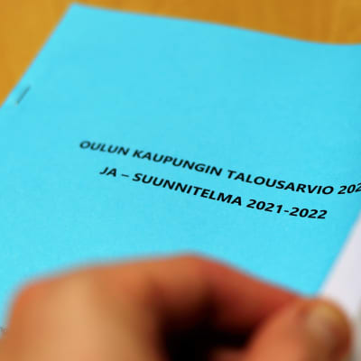Käsi selailee Oulun talousarvio -vihkoa.