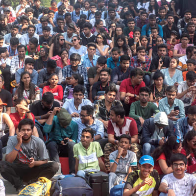 En stor grupp indiska studerande sitter som publik på ett utomhusevenemang.