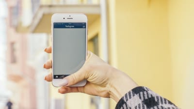 En hand håller i en telefon med applikationen Instagram öppen.