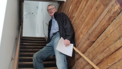En äldre man står uppe i en trappa och tittar neråt.