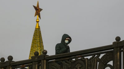 En människa med svart huva och munskydd promenerar förbi Kreml i Moskva där en röd stjärna pryder tornets topp.