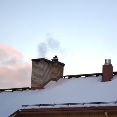Ett snötäckt tak med en skorsten varifrån det kommer rök.