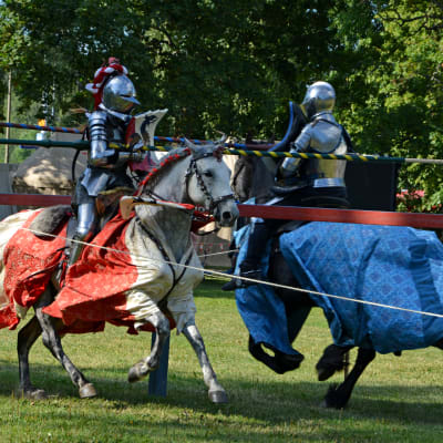 Två riddare i rustningar rider mot varandra med lansarna mot varandra i ett tornerspel
