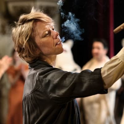 Närbild på Tove (Alma Pöysti) som har en cigarett i munnen samtidigt som hon målar en tavla.