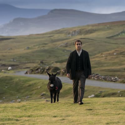 En man och en åsna som promenerar över en irländsk slätt med berg i bakgrunden.