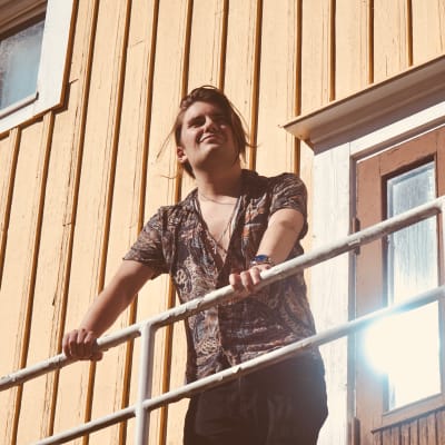 Musikern André Linman utomhus på en trappavsats, tittar upp mot solen.