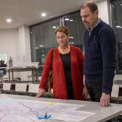 En kvinna och en man står vid ett bord och tittar på en karta över ett område som ska detaljplaneras.