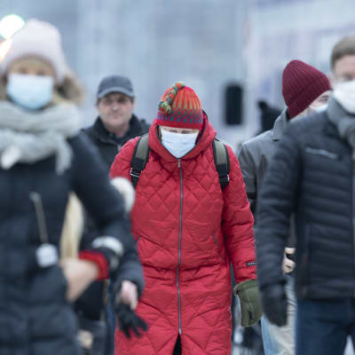 Människor i munskydd går i ett vinterklätt Helsingfors.