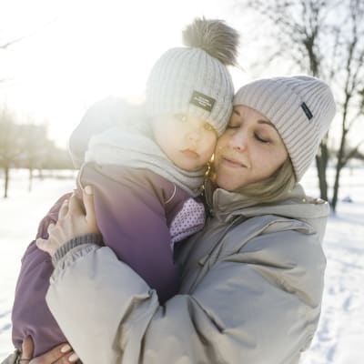 En mamma håller sin dotter i famnen på en solig vinterdag