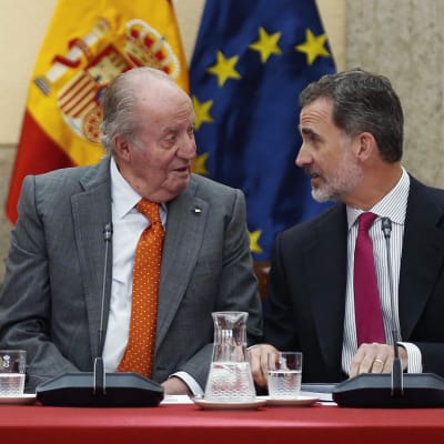 Juan Carlos och Felipe VI sitter bredvid varandra och ser på varandra.