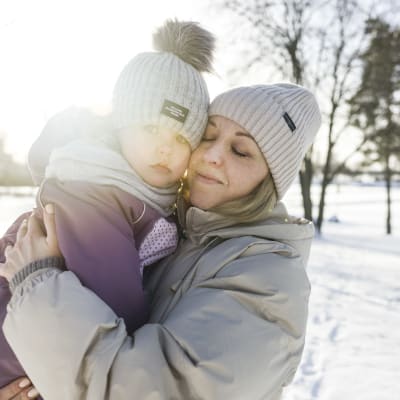 En mamma håller sin dotter i famnen på en solig vinterdag