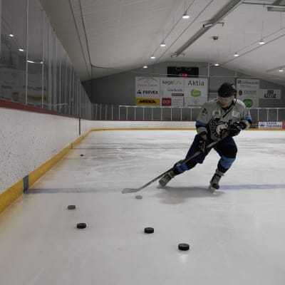 Ishockeyspelaren Don Lindgren skrinnar på isen omgiven av puckar. 