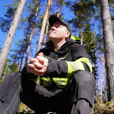 Thomas Lindholm sitter i skogen och tittar uppåt.