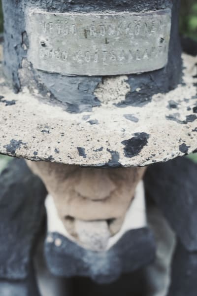 Staty med cylinderhatt på huvudet, på hatten en skylt med texten "Veijo Rönkkönen, 5930 Koitsanlahti."
