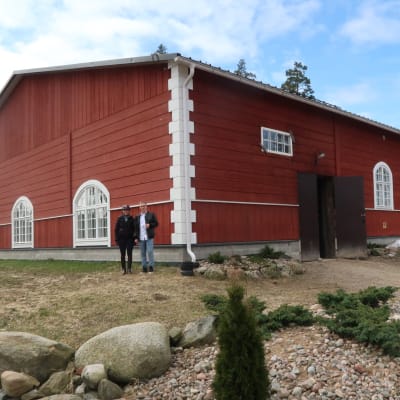 två personer framför ett stort rött ridhus med vackra valvbågade fönster i halvsoligt vårväder