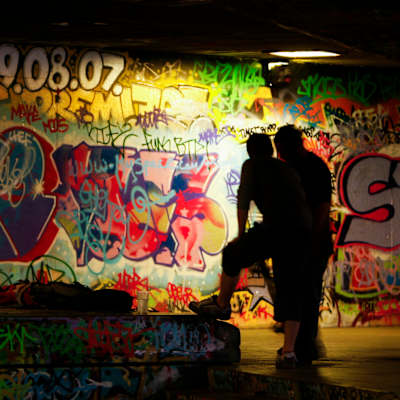 Två personer i står vid en graffitimålad vägg.