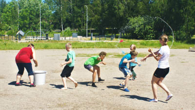 Barn på en sandplan kastar vattenballonger på varandra.