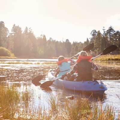 En flicka och en kvinna paddlar i en lugn naturskön vik i solsken.