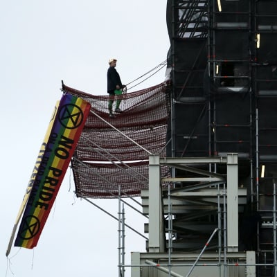 Man i Boris Johnson-peruk uppklättrad i tornet på Big Ben. Regnbågsfärgad flagga hänger i en byggställning.