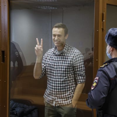 Aleksei Navalnyi näyttää voitonmerkkiä lasiseinän takana
