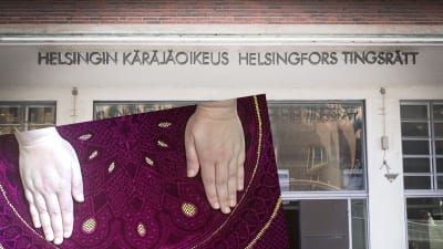Två händer på en matta inklippt framför Helsingfors tingsrätts byggnad.