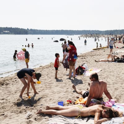 Människor solbadar på en badstrand i Solvik i Nordsjö, Helsingfors den 20 juni 2021.