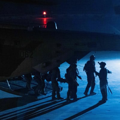 Sotilaita pimeässä sinisessä vastavalossa lentokoneen vierellä.