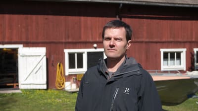 Martin Snickars står framför en röd gammal ladeugårdf på Husö