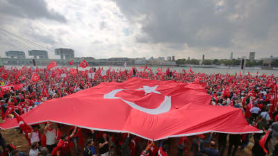 Demonstranter breder ut på en stor turkisk flagga samtidigt som hundratals andra viftar på mindre turkiska flaggor under en stöddemosntration för Turkiets president Erdoğan i Köln.