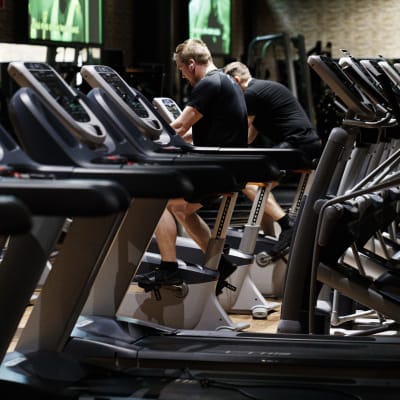 Två män sitter på konditionscyklar i ett tomt gym.