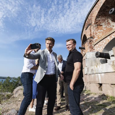 Två män tar en selfie framför en fästning med kanoner.