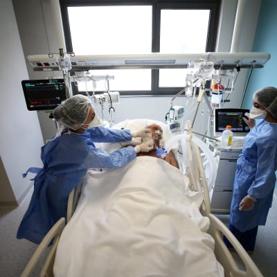 Två vårdare i coronautrustning står vid en patients säng.