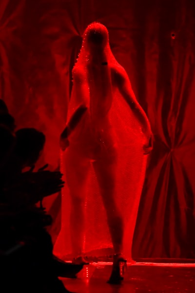 En modell poserar i en genomskilig slöja i rött ljus. 